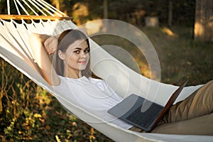 woman lies in a hammock with laptop on nature vacation travel