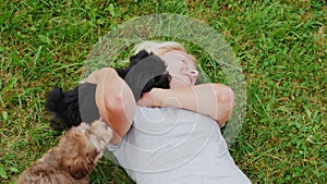 Woman lies on her back on the green grass, play with the puppies