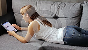 Woman lies with a tablet on the couch. Woman using tablet device with touch screen