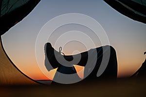 A woman lies in a tourist tent, crossing her legs and enjoying the sunset.