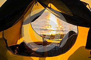 A woman lies in a tourist tent by the river and uses the phone