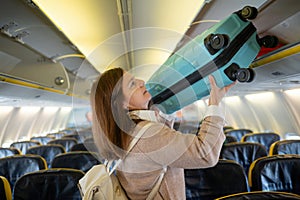 Woman lifting luggage into baggage compartment of airplane cabin