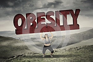Woman lifting obesity word in hills