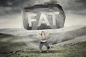 Woman lifts stone with fat word in hills