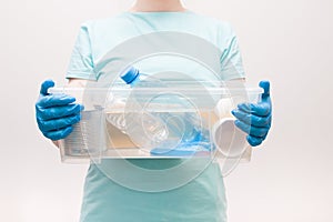 woman in a light blue t-shirt in blue disposable gloves holds a plastic container with waste for recycling, waste-free life style,