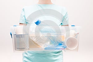 woman in a light blue t-shirt holds a plastic container with waste for recycling, waste-free life style, plastic bottles, a light