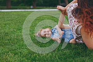 Woman in light dress and smiling little cute child baby girl lie on green grass in park rest play and have fun. Mother