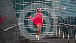 An woman with light pink hair descends the stairs on the street in the afternoon against the background of skyscrapers