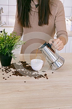 Woman in a light scandinavian kitchen pours coffee from a coffee machine into a mug