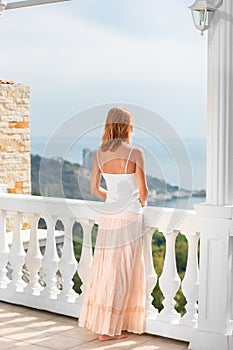 Woman in light summer dress standing on the balcony and enjoyin