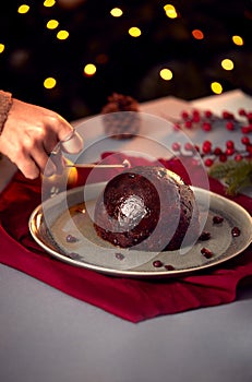 Woman Lighting Brandy Soaked Christmas Pudding On Table Set For Festive Christmas Meal