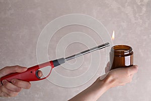 Woman lighting candle with gas lighter against grey wall, closeup