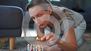 Woman lighting candles on birthday cake, celebrating birthday at home alone