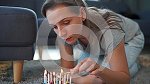 Woman lighting candles on birthday cake, celebrating birthday at home alone