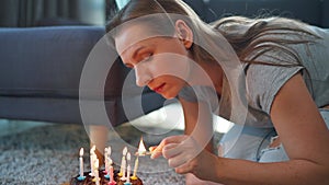 Woman lighting candles on birthday cake, celebrating birthday at home. Slow motion