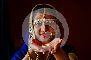 Woman lighting diyas with nuth nath nose piercing and the golden teak with traditionak fashion sari