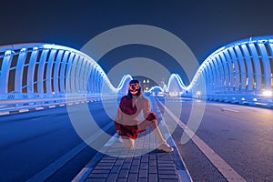 Woman with lighting neon glow mask on Meydan Bridge and street road or path way on highway in Dubai Downtown at night, urban city