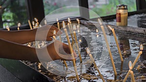 Woman lighting prayer candle aka offering, sacrificial or memorial candles lit in a church