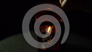 A woman lights a candle from a match in a red flashlight on a black background.