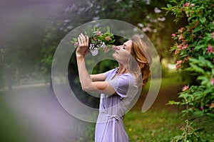 Woman in lilac dress sniffs bouquet of flowers with closed eyes and blurred spring colorful background