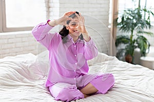 Woman in lilac pajamas sitting on bed