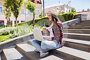 Woman with limonade sitting on the city stairs and using laptop