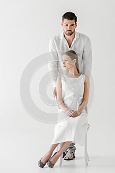 woman in linen white dress looking away sitting on chair while her boyfriend standing behind