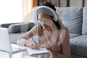 Woman listen audio course through headphones makes notes in copybook