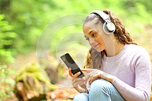 Woman listening music wathing phone content in a forest