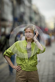 A woman is listening to music on her headphones on a crowded street.