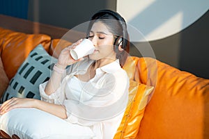 Woman listening to music on sofa relaxing and drinking coffee at home