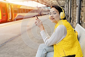 woman listening to music via headphones at railway station Travel with music Enjoying travel concept