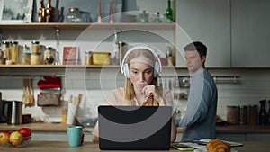 Woman listening training course sitting on kitchen with laptop headphones