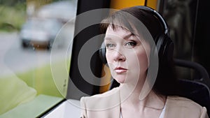 a woman listens to music with headphones on her smartphone while traveling by bus