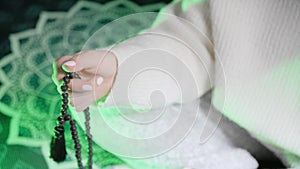 Woman, lit hand close up, counts Malas, strands of black lava beads used for keeping count during mantra meditations