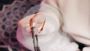 Woman, lit hand close up, counts Malas, strands of lava beads used for keeping count during mantra meditations.