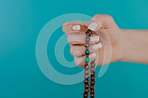 Woman lit hand counts mala beads strands of gemstones used for keeping count during mantra meditations. Blue background