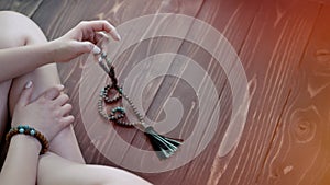 Woman lit hand counts mala beads strands of gemstones used for keeping count during mantra meditations. Lady sits on