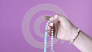 Woman lit hand counts mala beads strands of gemstones used for keeping count during mantra meditations. Pink background