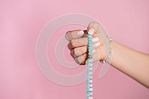 Woman lit hand counts mala beads strands of gemstones used for keeping count during mantra meditations. Pink background
