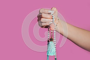 Woman lit hand counts mala beads strands of gemstones used for keeping count during mantra meditations. Pink background