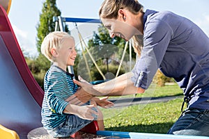 Woman and little boy chuting down slide at playground