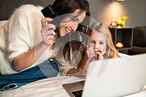 Woman and little daughter with laptop and credit card making online reservation of hotel room