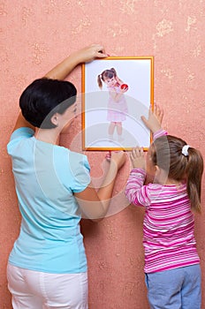 Woman with little girl hang up a picture