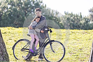 A woman and a little girl - her daughter - are hugging each other while sitting on a bicycle