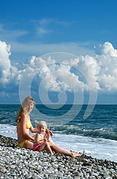 Woman and little girl sit on seacoast