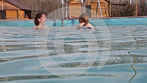 Woman and the little girl swims in the outdoor pool