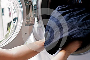 Woman loading black fabric jeans pant into washing machine by hand for clean