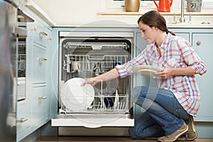 Woman Loading Dishwasher In Kitchen