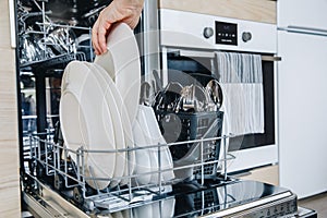 Woman loading the dishwasher. Open dishwasher with clean glasses and dishes close-up after washing